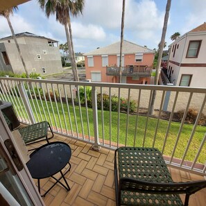 A balcony with two chairs and a table, overlooking a residential area with houses and a well-maintained lawn.