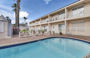 A hotel with a swimming pool, lounge chairs, and a fenced patio area.