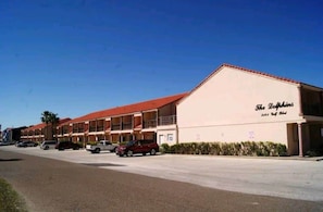 A motel with a red roof and multiple balconies, located on a street with parked cars.