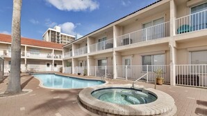 Un hotel con piscina y jacuzzi, rodeado de un patio de ladrillo y una palmera.
