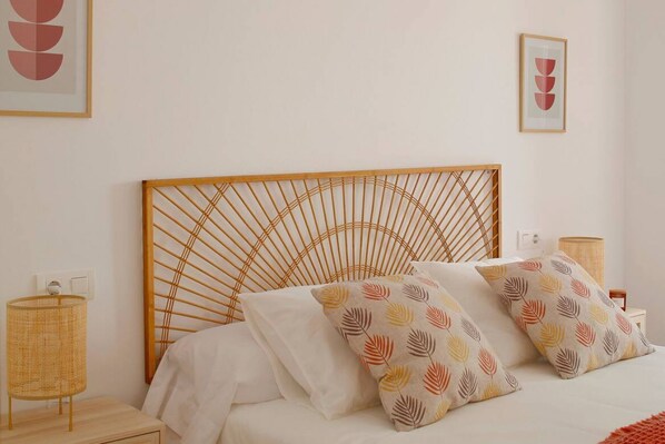 A bed with a wooden headboard, two patterned pillows, a bedside lamp, and a wall-mounted light switch.