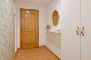 A hallway with a wooden door, a white wall with a mirror, and a shelf with candles.