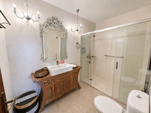 A bathroom with a white sink, wooden vanity, a large mirror, a glass shower enclosure, and a white toilet. - Venetian Palace Chania (Chania)