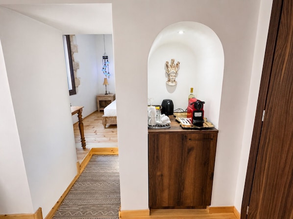 A narrow hallway leading to a room with a bed, a small table, a lamp, and a coffee machine. - Venetian Palace Chania (Chania)
