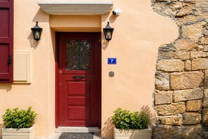 A red door with a number 7 sign, two wall-mounted lights, and a stone wall. - Venetian Palace Chania (Chania)
