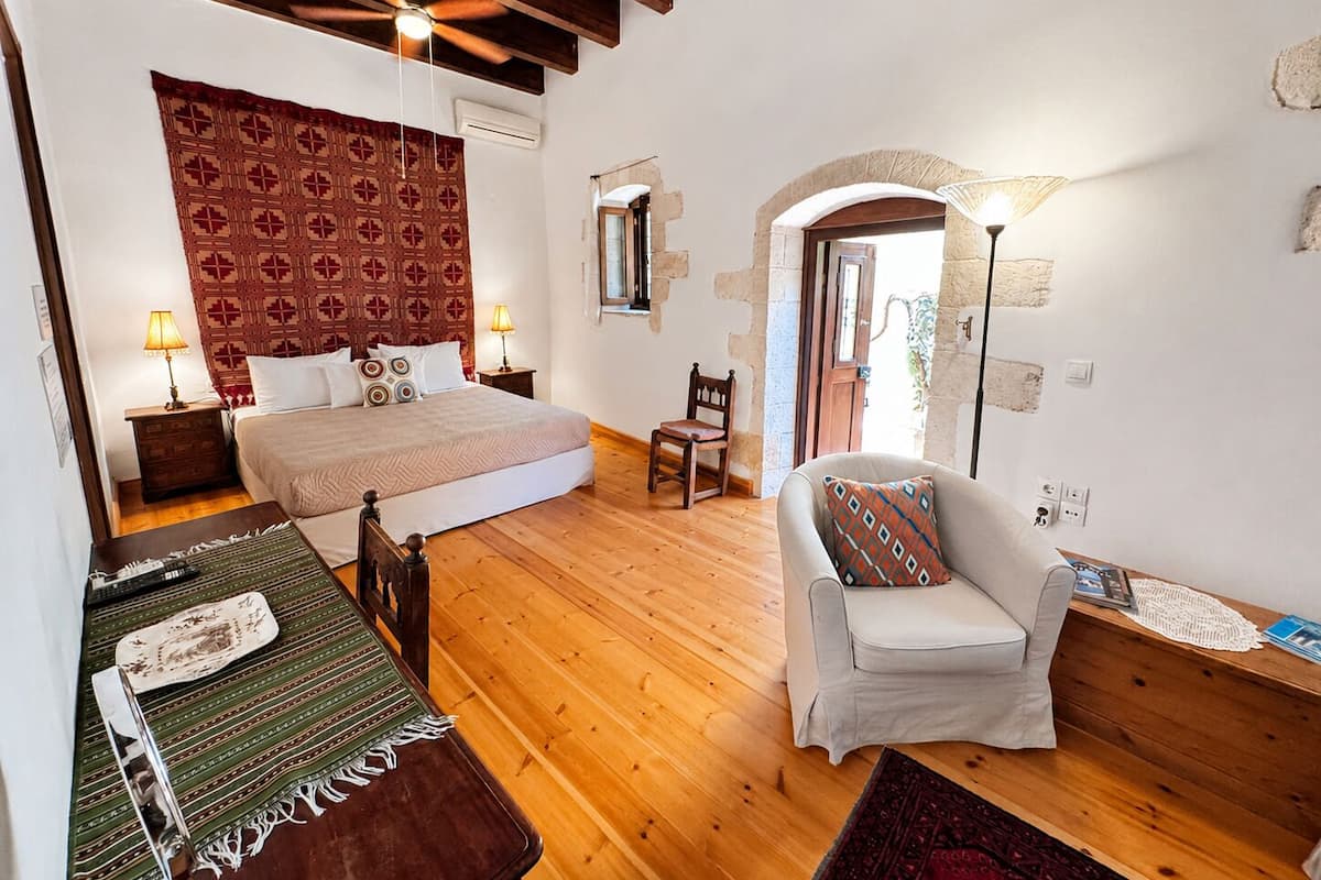 Quarto com cama, cadeira, mesa, luminária e porta que dá para outro cômodo.