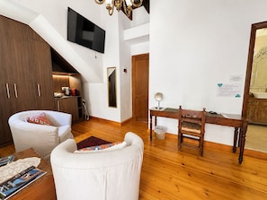 A modern living room with a flat-screen TV, wooden flooring, a sofa, a dining table with chairs, and a kitchen area with wooden cabinets. - Venetian Palace Chania (Chania)