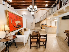 A cozy living room with a sofa, a wooden dining table, and a staircase leading to a kitchen. - Venetian Palace Chania (Chania)