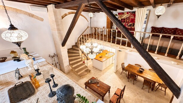 Un loft amplio con techo alto, vigas de madera a la vista, una escalera central, comedor y cocina.