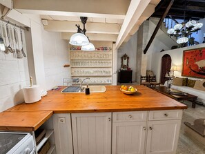 A kitchen with a wooden countertop, white cabinets, and a built-in sink. There are shelves with glassware and a decorative mirror. - Venetian Palace Chania (Chania)