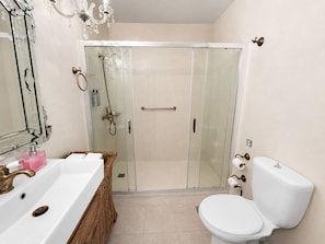 Ein Badezimmer mit weißem Waschbecken, Toilette, Duschkabine aus Glas und Spiegel mit aufwendiger Verzierung.
