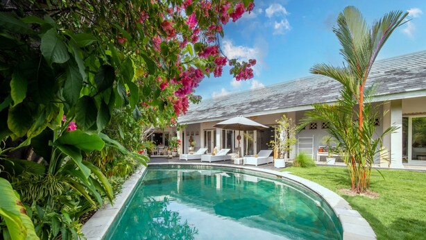A swimming pool with a surrounding garden, a covered outdoor seating area, and a house with a tiled roof.