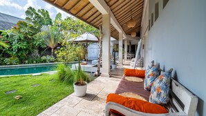 A covered patio with a pool, outdoor seating, and lush greenery.