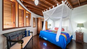 Une chambre à coucher avec un lit à baldaquin, un plancher en bois et un banc agrémenté de coussins.