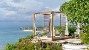 Une pergola en bois dotée d’un espace salon confortable, donnant sur une plage et l’océan.