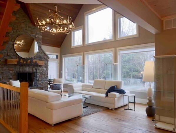 Relax in this inviting living room with a stone fireplace, two sofas, and a large window offering a view of the outdoors.