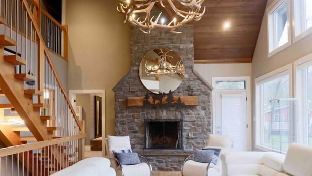 A spacious living room with a stone fireplace, white sofas, and a wooden staircase. - The Rowanwood - Muskoka Cottage Retreat (Huntsville)