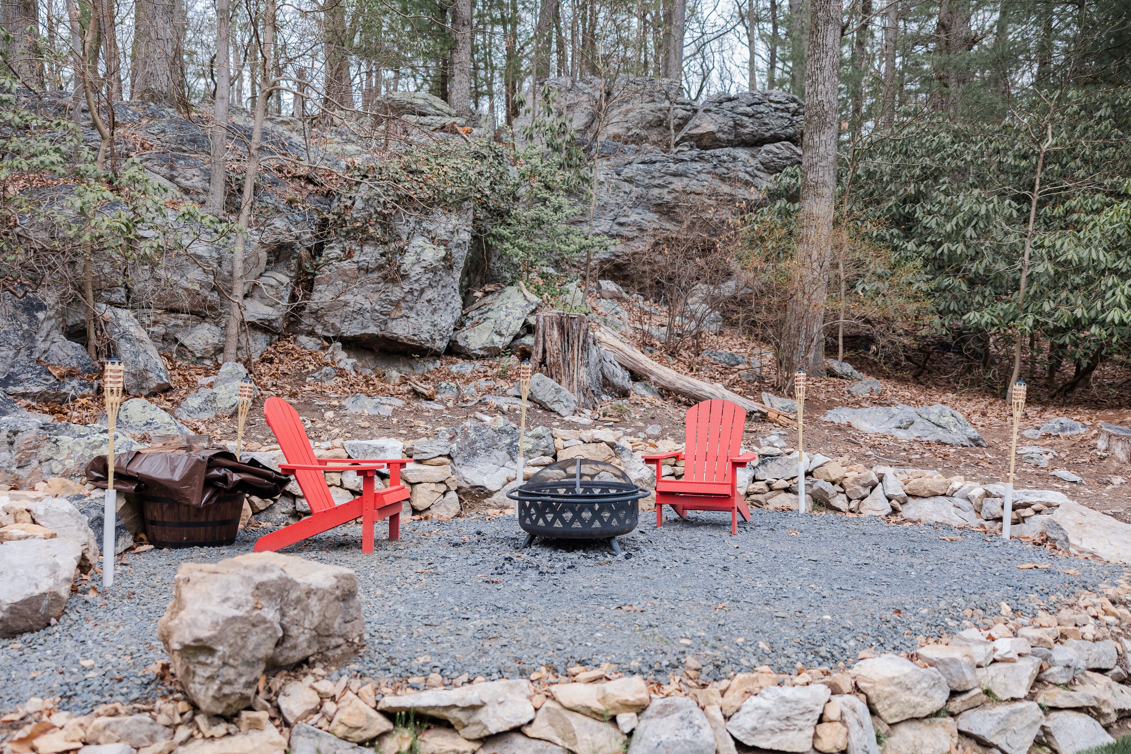 A campsite with two red Adirondack chairs, a fire pit, and a wooden bucket.