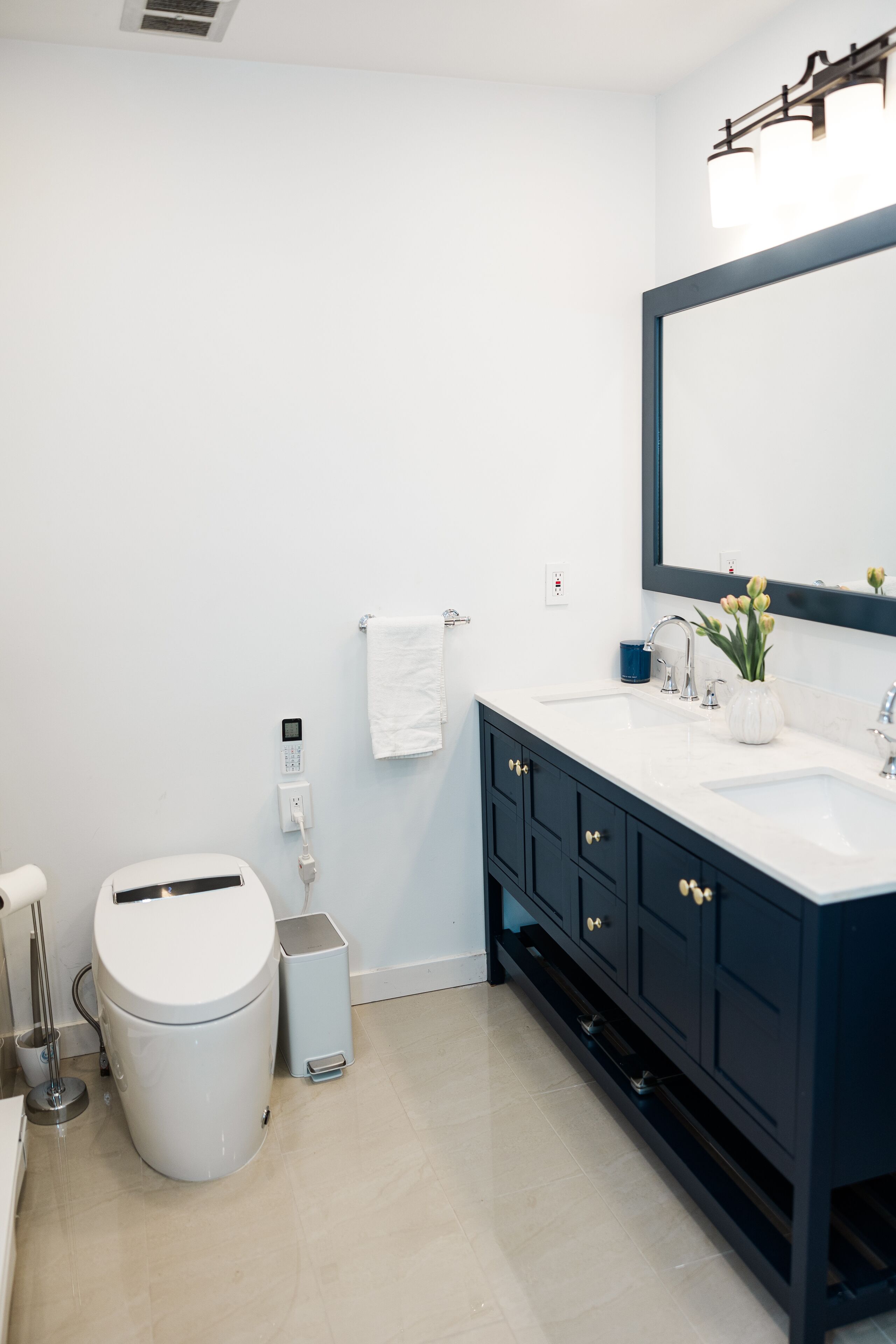 Een moderne badkamer met een wit toilet, een prullenbak, een wastafel met spiegel en een vaas met bloemen.