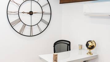 A room with a white desk, a black office chair, a large wall clock, and a globe on the desk.