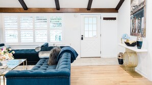 Uma sala de estar com um sofá azul escuro, uma porta branca e uma janela com persianas.