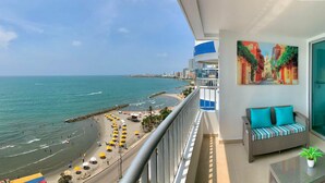 A balcony with a view of the beach and ocean, a sofa with cushions, and a painting on the wall. - 2P1-AL4 APARTAMENTO DE 2 ALC CON AIRE A. (Cartagena)