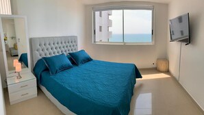 A bedroom with a large bed, a TV mounted on the wall, and a window with a view of the sea. - 2P1-AL4 APARTAMENTO DE 2 ALC CON AIRE A. (Cartagena)