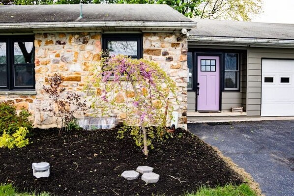 A stone house with a garden, a purple door, and a garage.