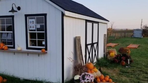 A small white building with a dark roof, windows with black frames, and a porch area with pumpkins and other produce. - Cozy farmhouse with views and amenities! Pet-friendly, baby goats and chickens! (Grantville)