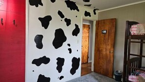 A room with a cow print wall, a red door, a wooden door, and a bunk bed with a plaid blanket. - Cozy farmhouse with views and amenities! Pet-friendly, baby goats and chickens! (Grantville)