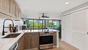 Een moderne keuken met houten kastjes, een inbouwoven en een groot raam met uitzicht op een tuin.