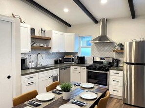 Une cuisine moderne avec des meubles blancs, un réfrigérateur en acier inoxydable, une cuisinière à gaz et un four à micro-ondes.
