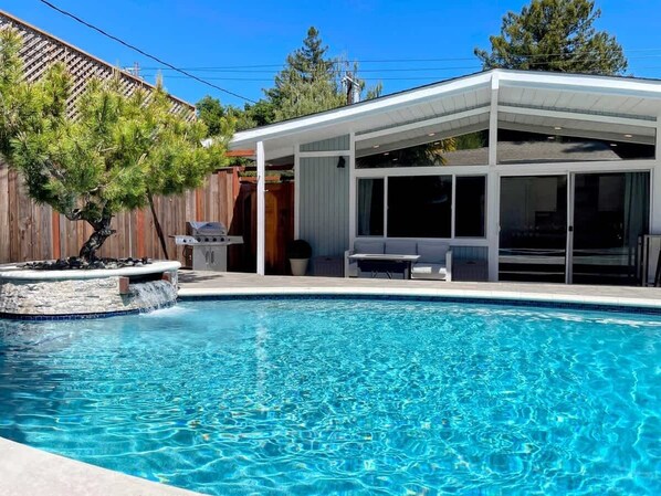 Une piscine avec un patio couvert, une clôture en bois et un arbre.