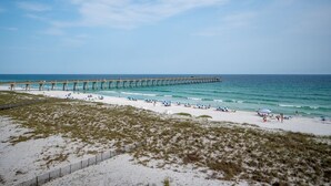 A beach with a wooden pier extending into the ocean, sandy beach, and people relaxing.