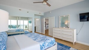 A bedroom with a bed, a dresser, a ceiling fan, and a TV on the wall.