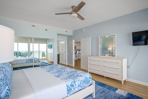 A bedroom with a bed, a dresser, a ceiling fan, and a TV on the wall.