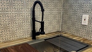 Una cocina con un lavamanos de acero inoxidable, una tabla de cortar de madera y una toalla colgada en la encimera.