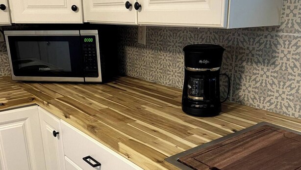 Una cocina con armarios blancos, microondas, cafetera y encimera de madera.