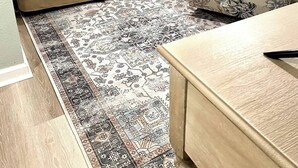 Una sala de estar con un sofá color beige, un sillón estampado, una mesa de centro de madera y un tapete decorativo.