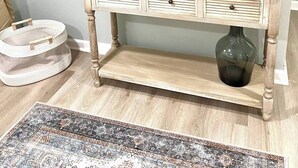 Un televisor sobre una mesa consola de madera con cajones, un florero y una alfombra estampada.