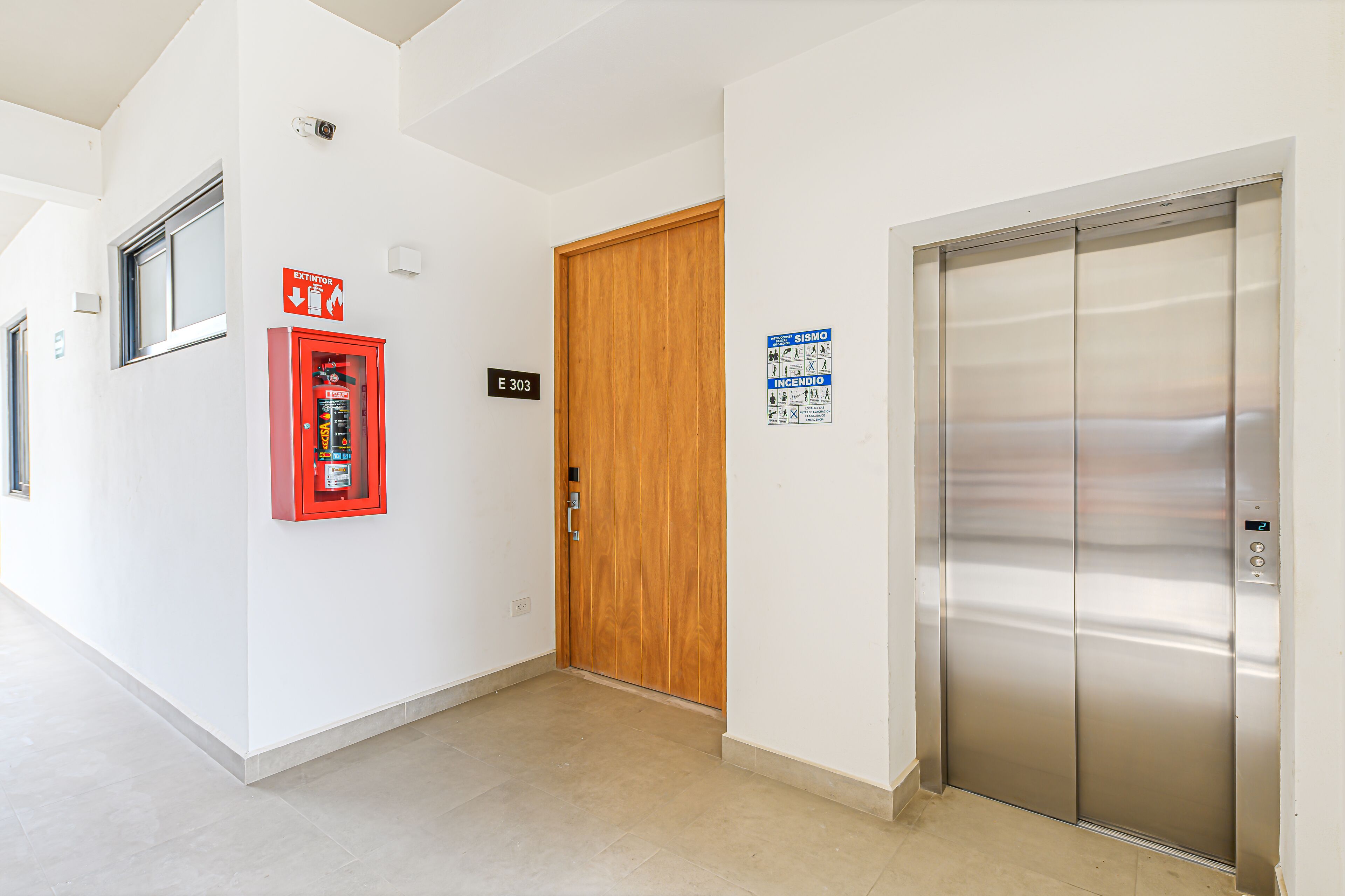 A hallway with a fire extinguisher, an elevator, and a wooden door marked E303.
