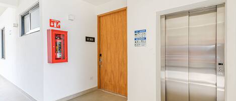 A hallway with a fire extinguisher, an elevator, and a wooden door marked E303.