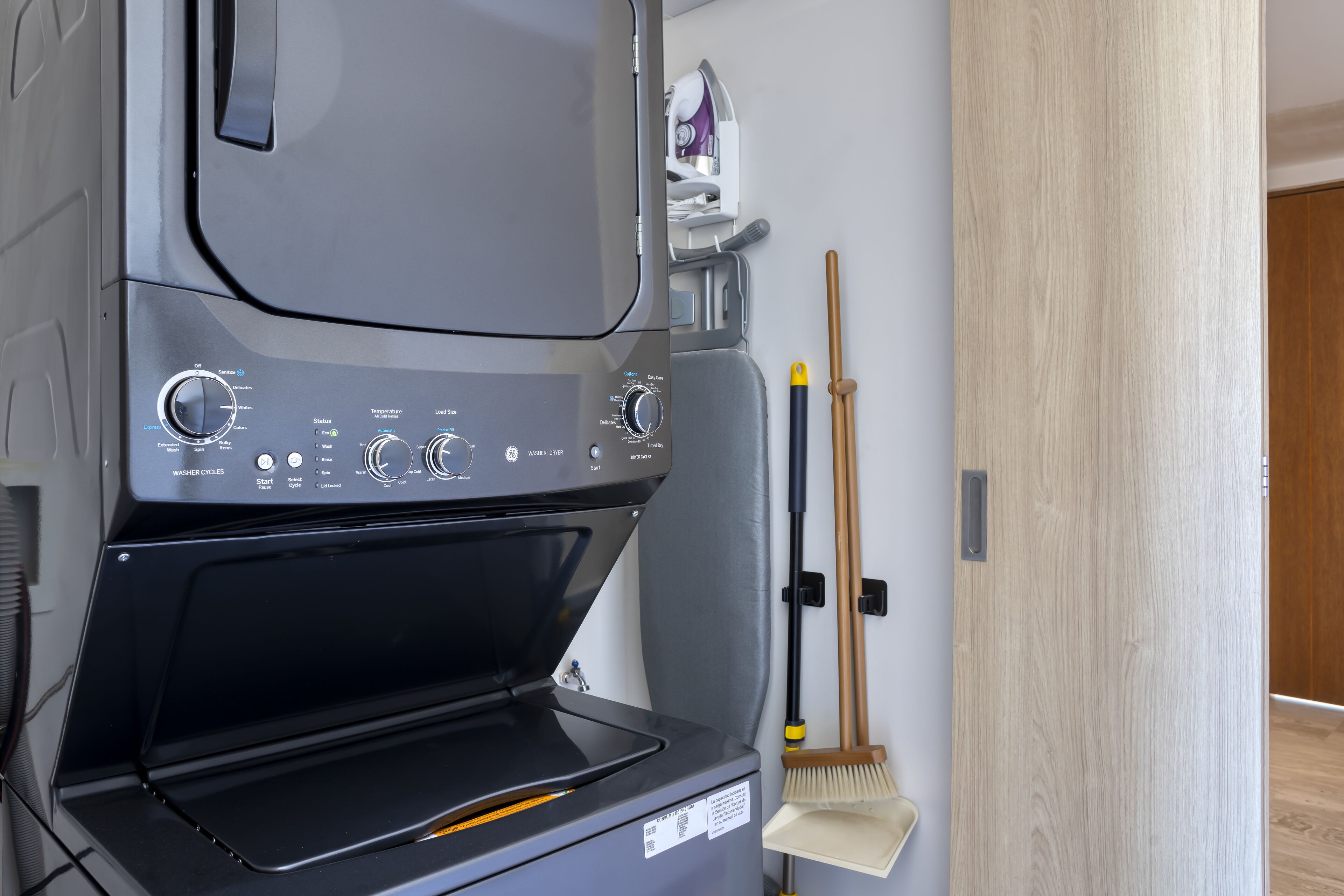 A modern kitchen with a built-in washer-dryer unit, a broom, and a mop.