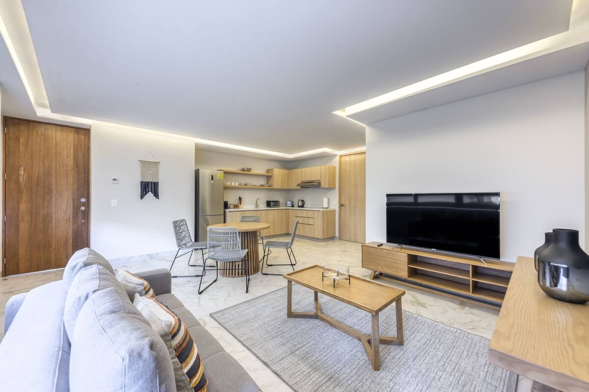 A modern living room with a sofa, coffee table, TV, and kitchen area.