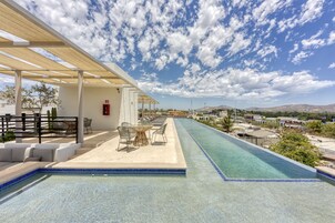 Zona de piscina con sillones de descanso y una mesa, un espacio de estar cubierto y vistas del paisaje circundante.