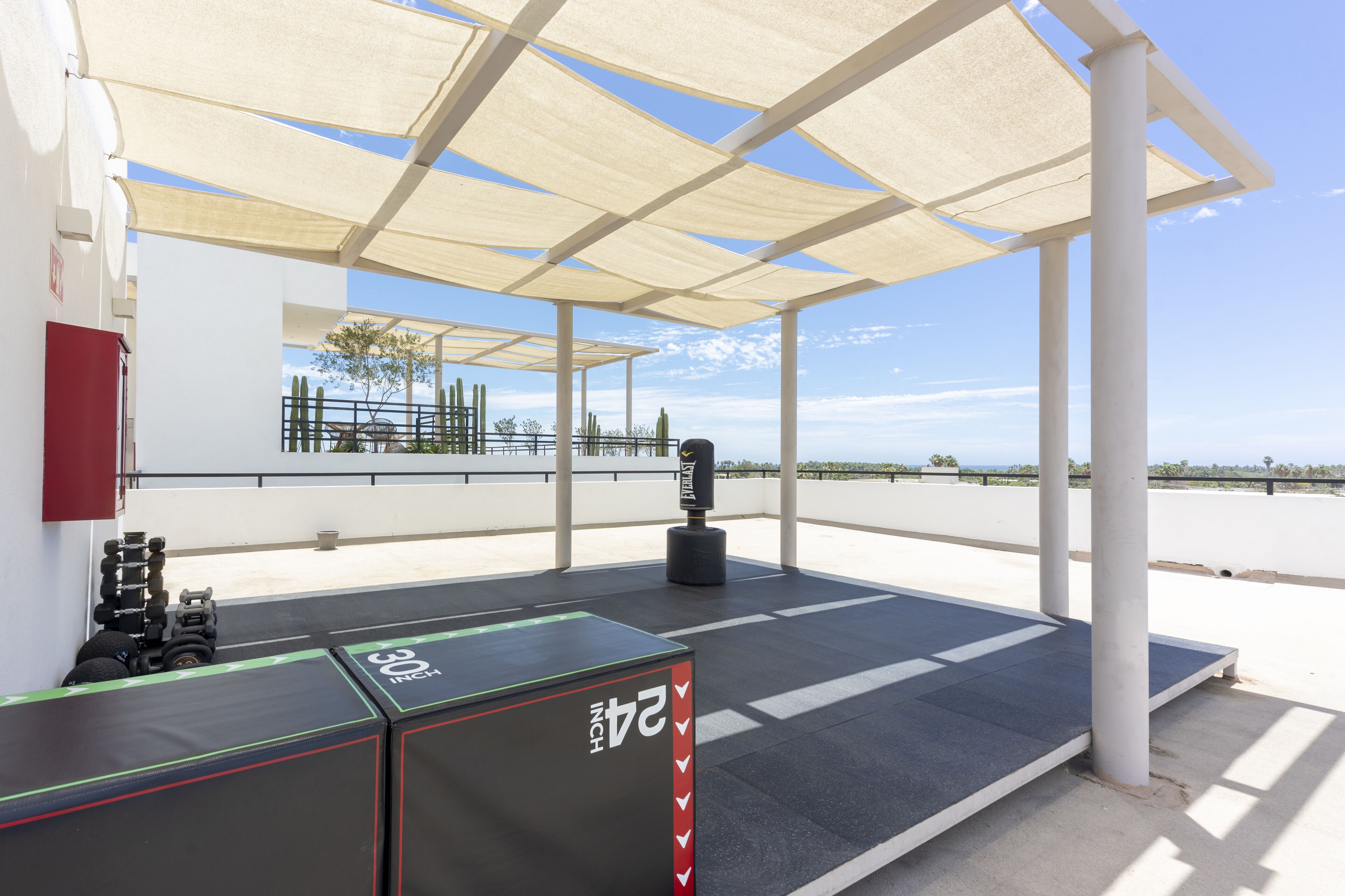 An outdoor gym area with exercise equipment, a shaded canopy, and a view of the desert landscape.