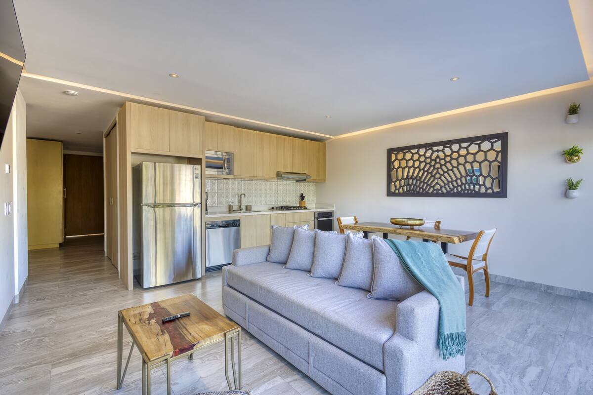 A modern living room with a grey sofa, wooden coffee table, and a dining area with a wooden table and chairs.
