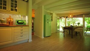 A kitchen with white cabinets, a green microwave, and a green refrigerator. There is a dining area with a table and chairs. - Casa da Luz Charming Cottage w/ Beautiful Garden (Vila Nova de Cerveira)