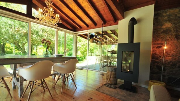 A modern interior with a large dining table, white chairs, a stone wall, and a wood-burning stove. - Casa da Luz Charming Cottage w/ Beautiful Garden (Vila Nova de Cerveira)