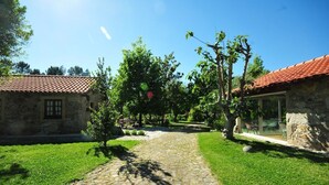 A stone building with a red-tiled roof, a cobblestone pathway, and a well-maintained lawn. - Casa da Luz Charming Cottage w/ Beautiful Garden (Vila Nova de Cerveira)